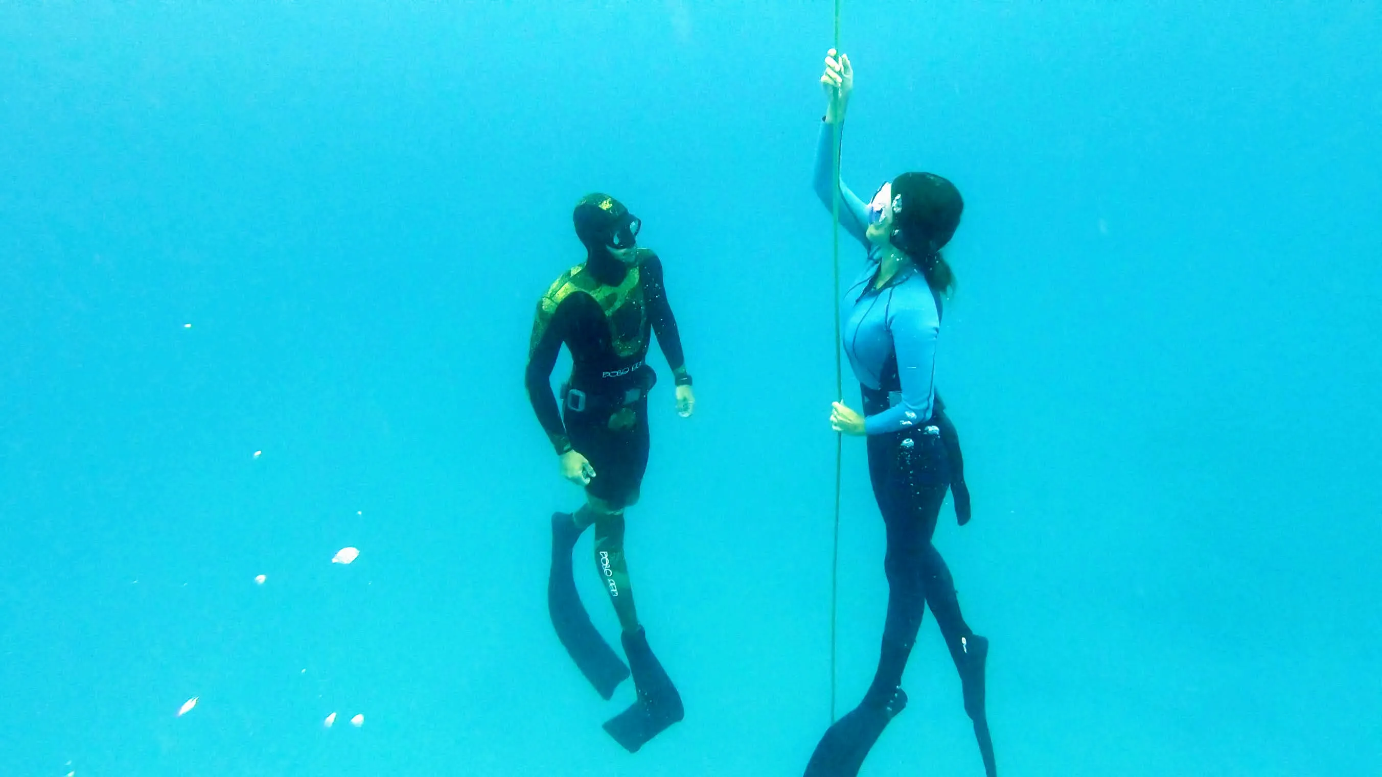 Dos apneístas junto al cabo en agua turquesa, uno sujeta la cuerda.