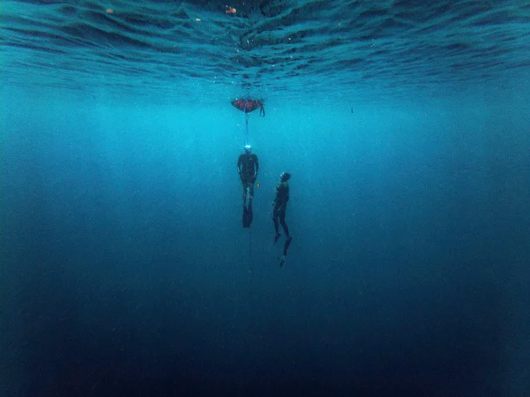 Two freedivers deep in the blue, seen from the surface.