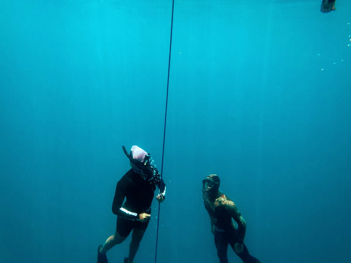 Two freedivers descending along the guide line, one following the other.