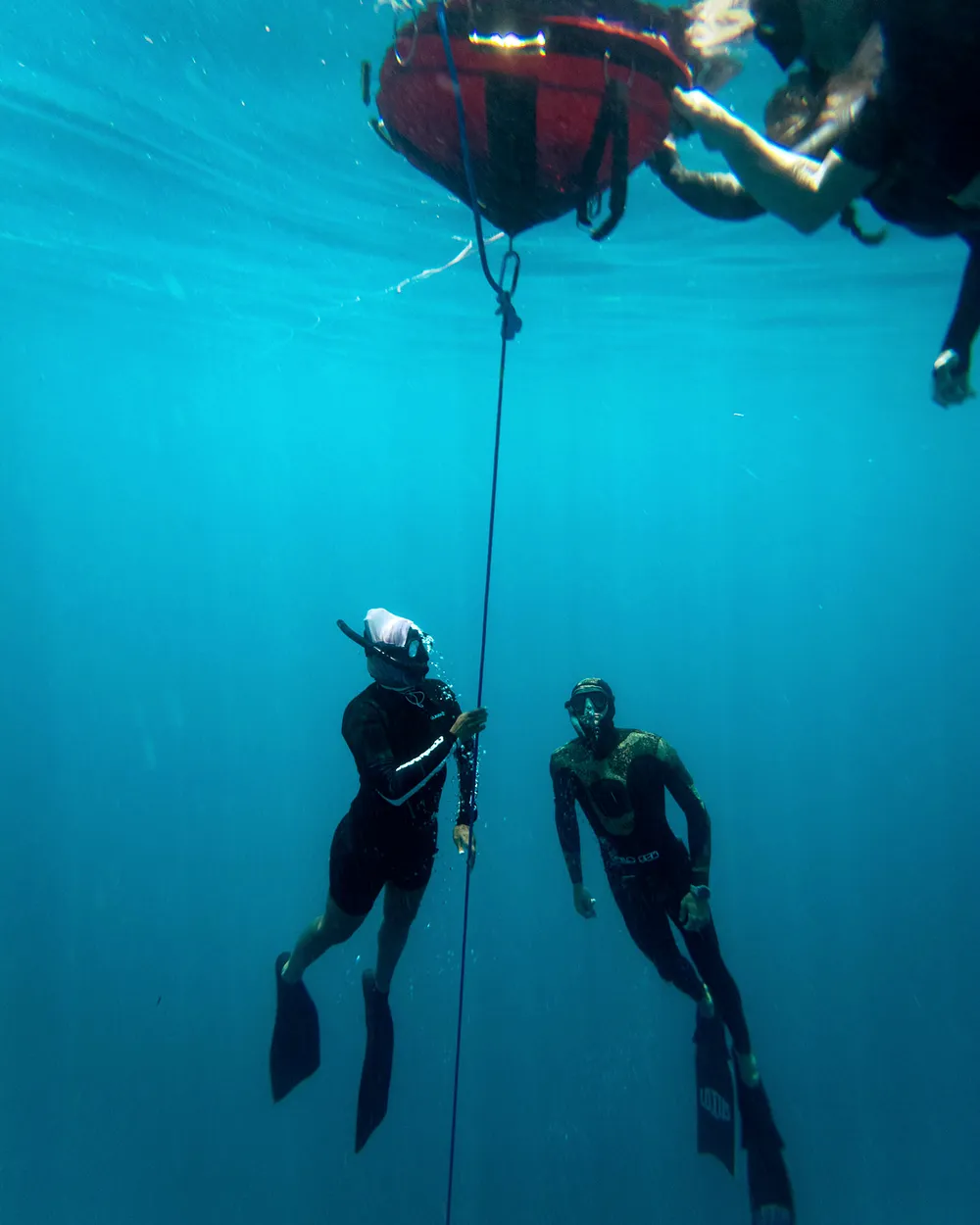 Two freedivers descending along the line under the buoy.